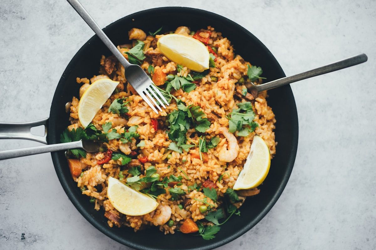 Skillet of golden rice with shrimp, peas, carrots, lemon wedges and cilantro