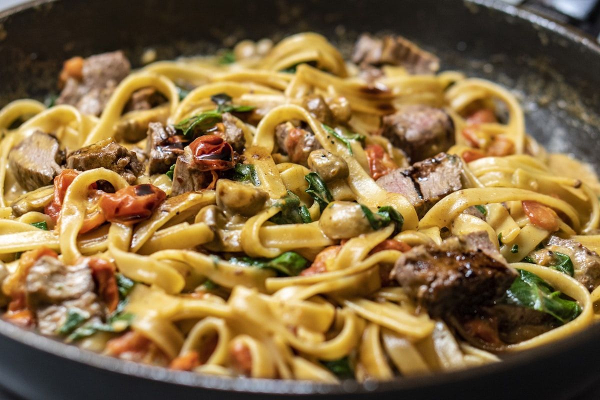 Pan of creamy fettuccine with seared steak pieces, spinach and tomatoes