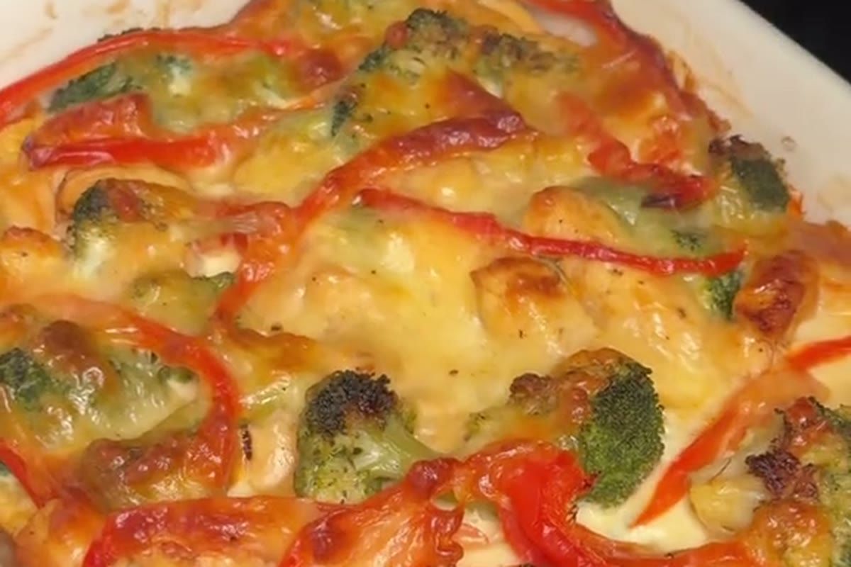Baked broccoli and chicken casserole with red peppers and melted cheese in a white dish