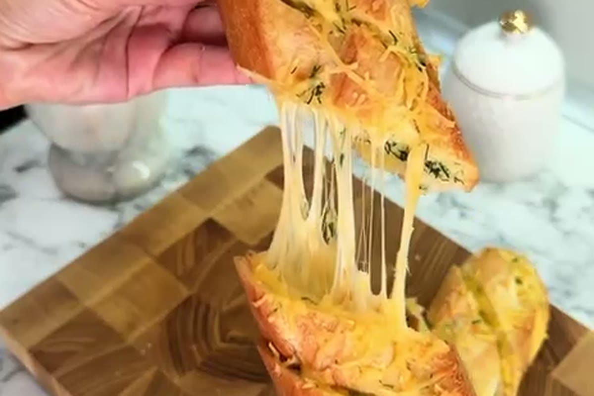 Slice of garlic cheese baguette lifted from a wooden board with melted cheese pulling